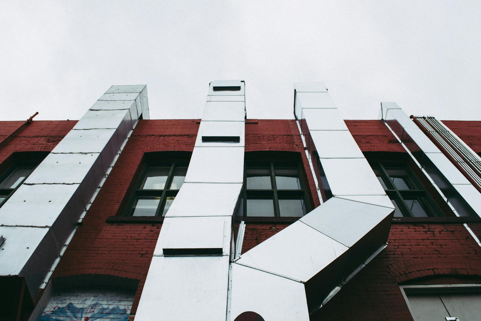 Duct leakage testing — exterior commercial building with rectangular sheet metal duct riser on red brick facade