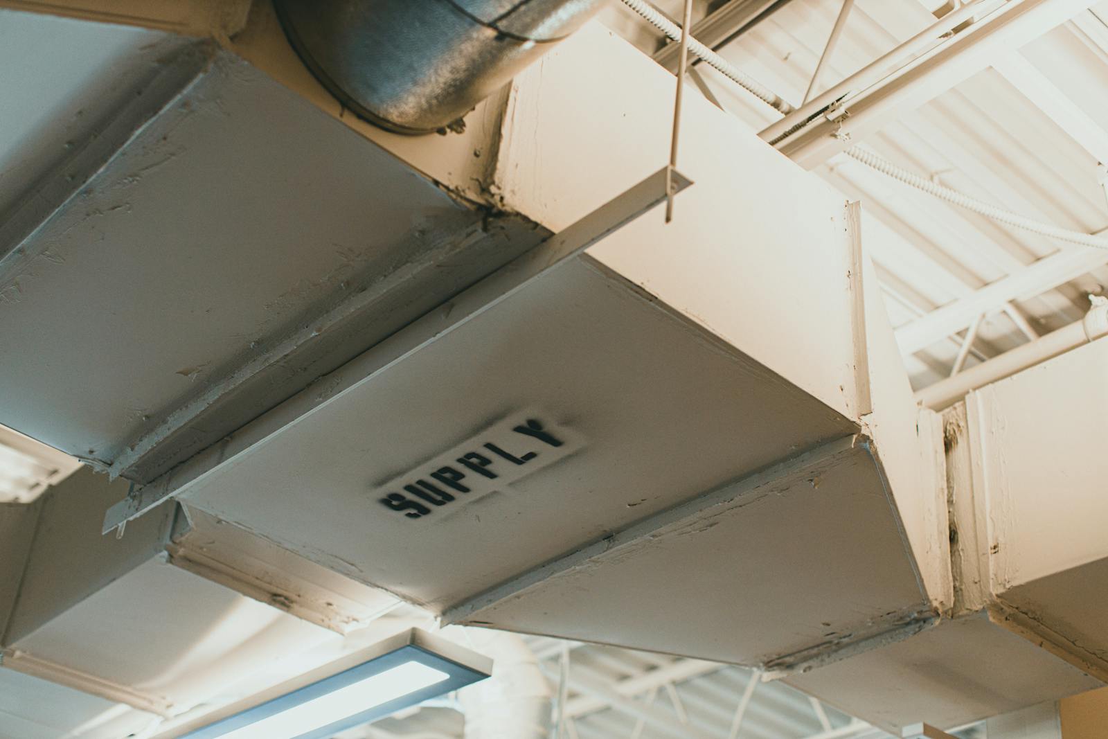 Duct leakage testing — commercial supply duct labeled SUPPLY at ceiling, the kind of seam tested under SMACNA Class A/B/C