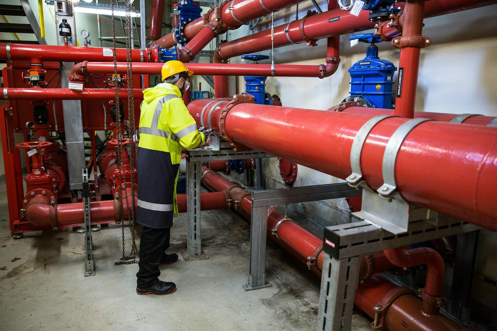 Hydronic water balancing — engineer in hi-viz PPE inspecting a red commercial hydronic piping system