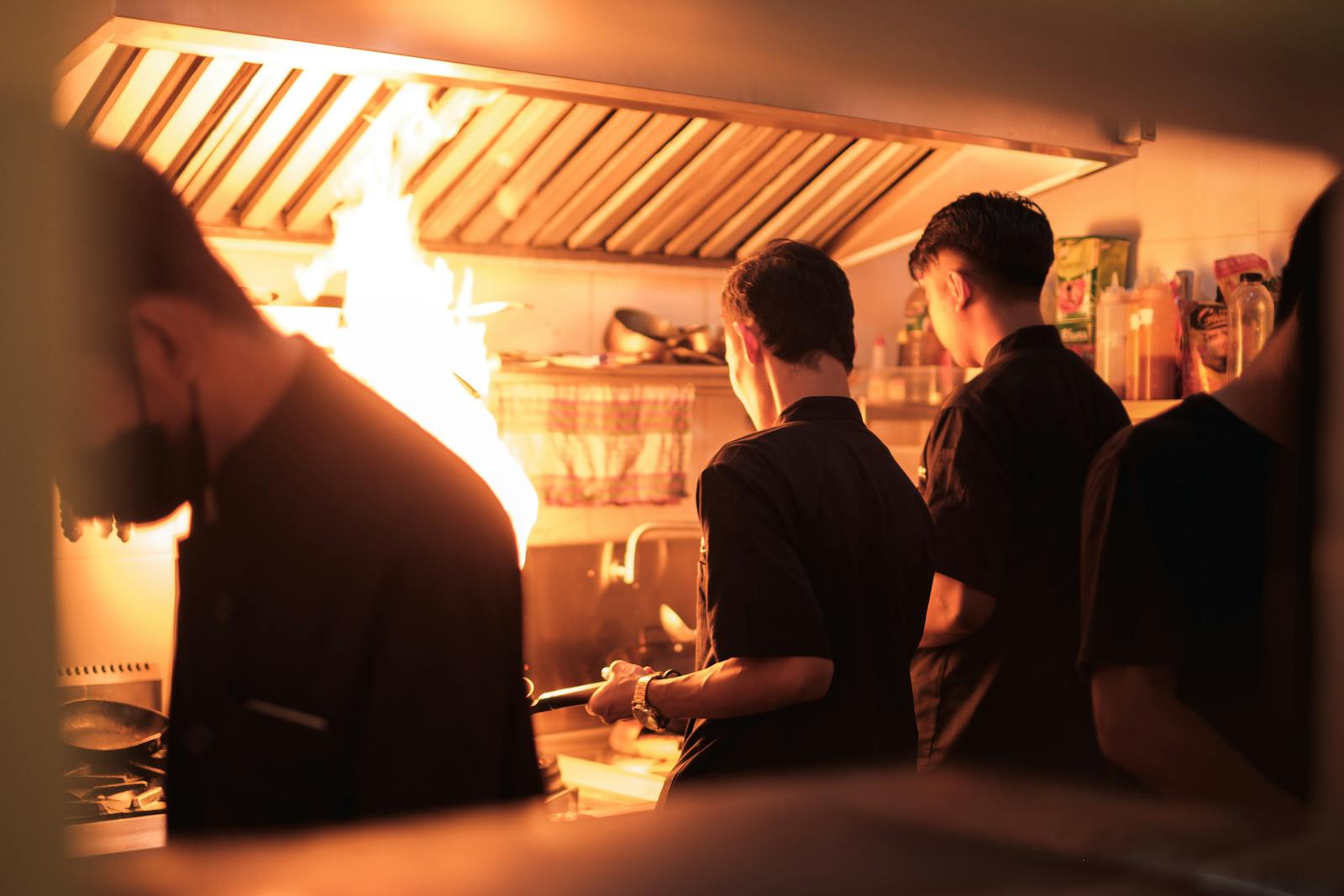 Kitchen hood and makeup air (MUA) testing — chefs cooking with flames in a commercial kitchen, the cooking heat load that drives exhaust and MUA capacity